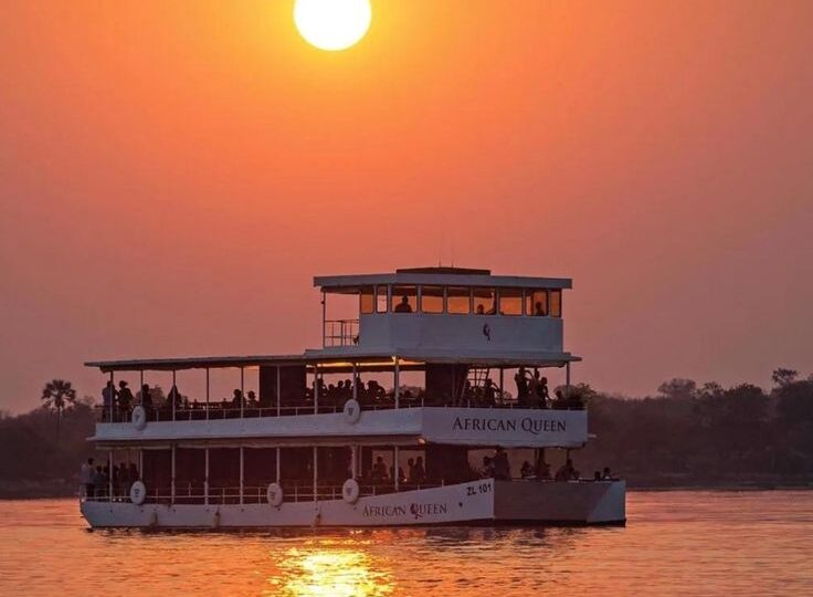 The African Queen luxury boat cruising on a calm river at sunset with a giant orange sun in the background in river nile uganda by excellent african safaris.